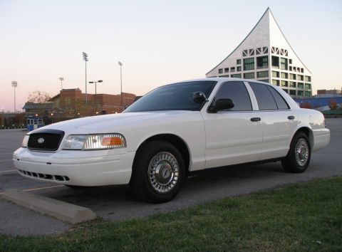 2001 Ford Crown Victoria - A white 2001 Ford Crown Victoria sedan is parked in front of a modern building.