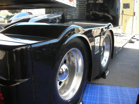 1998 Ford Crown Victoria - glossy black fender arches over polished aluminum dual wheels with a chrome hub cap on a custom truck or coach.