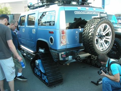 1998 Ford Crown Victoria - lifted blue Hummer H2 on rubber track systems draws onlookers and a photographer at an outdoor Toyo Tires event.