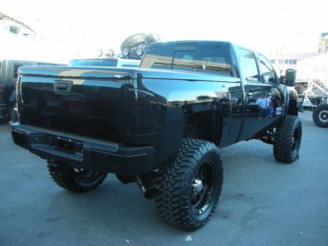 1998 Ford Crown Victoria - Rear quarter view of a glossy black lifted crew-cab pickup with a bed rack and large black off-road wheels.
