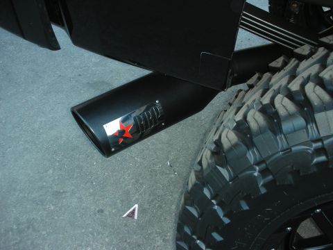 1998 Ford Crown Victoria - black angled exhaust tip bearing a red star emblem extends near a large mud-terrain off-road tire.