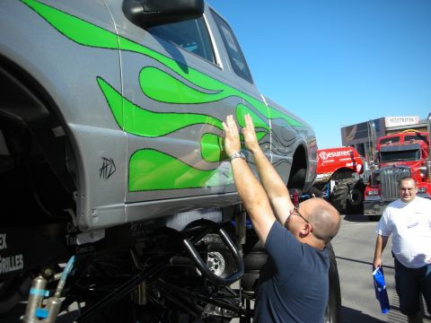1998 Ford Crown Victoria - man reaches up to the green-flamed silver body of a tall lifted truck while another person looks on at an outdoor show.