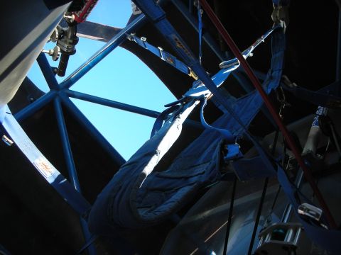 1998 Ford Crown Victoria - Looking up through a blue tube-frame roll cage at a folded fabric race seat and harness belts against a clear sky.
