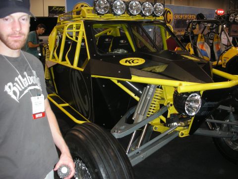 1998 Ford Crown Victoria - yellow tube-frame off-road buggy with a roof-mounted light bar and KC lights on display as a man stands beside it indoors.