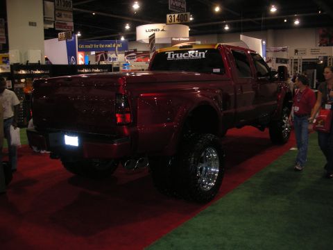 1998 Ford Crown Victoria - Rear three-quarter view of a lifted maroon Ford dually pickup with dual rear wheels and chrome rims at an indoor expo.