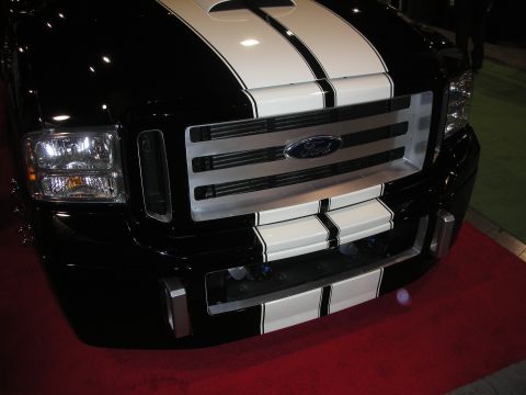 1998 Ford Crown Victoria - Close-up of a black Ford truck front end painted with twin white racing stripes over the hood and Ford-badged grille.