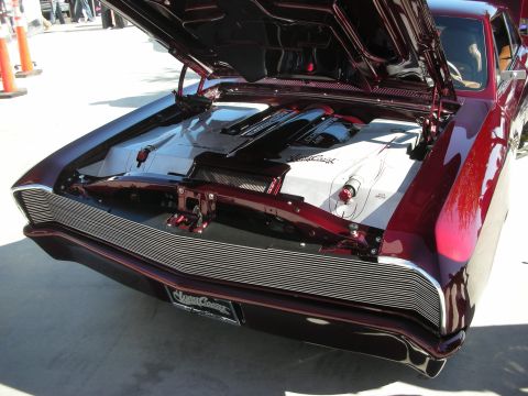 1998 Ford Crown Victoria - Rear of a deep maroon custom car with the trunk lid raised, exposing a chrome-detailed engine and a billet rear grille panel.