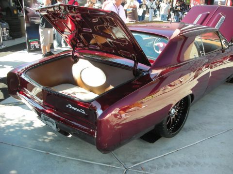 1998 Ford Crown Victoria - Rear three-quarter view of a maroon custom Corvair coupe with the engine lid open, lowered over chrome wheels among a show crowd.