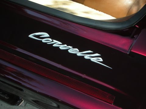 1998 Ford Crown Victoria - Close-up of a chrome 'Corvair' script badge mounted on a deep maroon metallic body panel above the rear reflector.