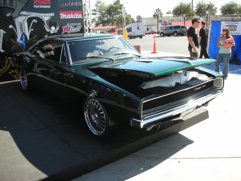 1998 Ford Crown Victoria - black custom Dodge Charger muscle car with chrome wheels and a green-striped hood displayed on a riser in an outdoor lot.