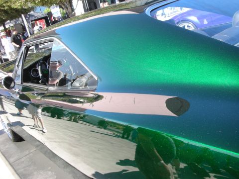 1998 Ford Crown Victoria - Detail of a green metallic-flake car body and side window, mirror-like paint reflecting people and trees at an outdoor show.