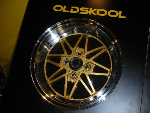 1998 Ford Crown Victoria - gold-finished multi-spoke 'Oldskool' alloy wheel with a polished lip mounted on a black display board at a show.