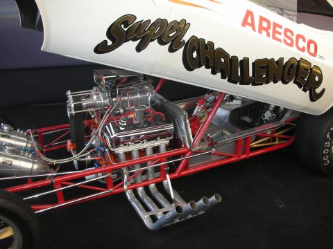1998 Ford Crown Victoria - blown chrome dragster engine on a red tube chassis beneath a tilted fiberglass body lettered 'Super Challenger' and 'Aresco'.