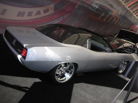 1998 Ford Crown Victoria - silver custom fastback muscle car on polished chrome wheels displayed at an indoor exhibition with a motion-blur backdrop.