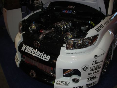 1998 Ford Crown Victoria - Heavily turbocharged engine bay of a white Scion xB show car covered in sponsor decals including K2 Motoring and Garrett.