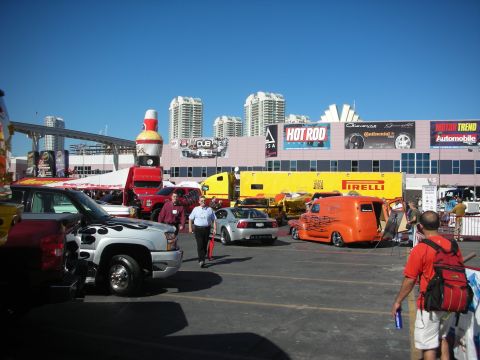1998 Ford Crown Victoria - Busy outdoor auto-show midway with vendor trucks, Pirelli and Hot Rod banners and casino high-rises under a clear sky.