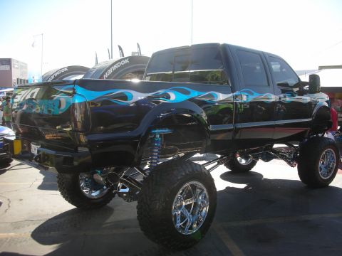 1998 Ford Crown Victoria - Black lifted crew-cab pickup with blue tribal flame graphics, chrome wheels and long-travel shocks at an outdoor show.