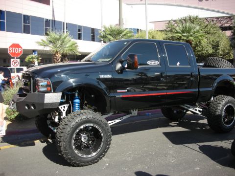 1998 Ford Crown Victoria - Black lifted Ford crew-cab pickup with a red pinstripe on big chrome wheels and long shocks, parked near a stop sign.
