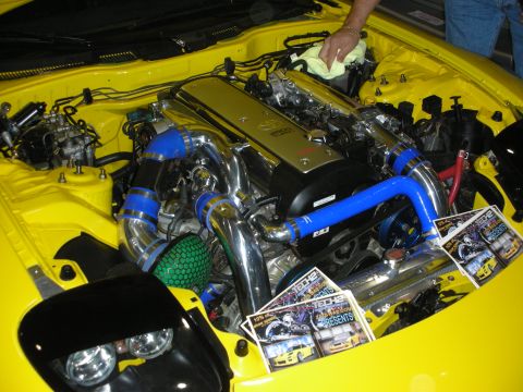 1998 Ford Crown Victoria - Detail of a modified yellow car's engine bay featuring a turbocharger, blue silicone hoses and polished intercooler piping at a show.