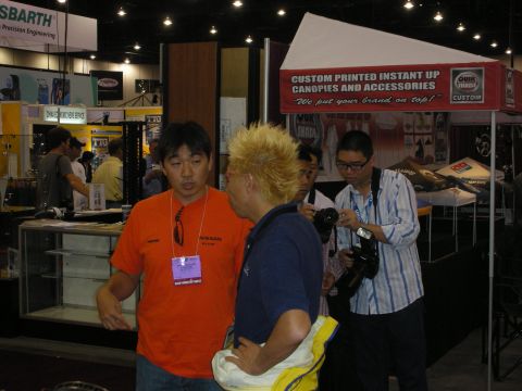 1998 Ford Crown Victoria - Attendees converse beside a vendor booth advertising custom printed instant-up canopies at an indoor trade show.