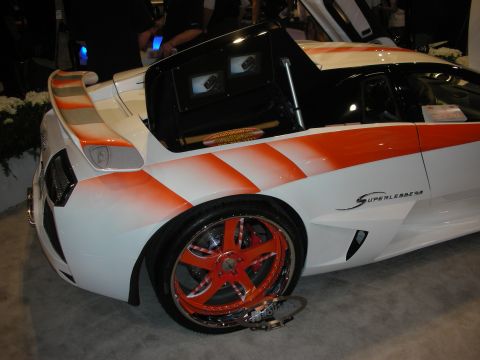 1998 Ford Crown Victoria - Rear three-quarter of a white-and-orange-striped supercar with chrome-lipped red wheels on display indoors.