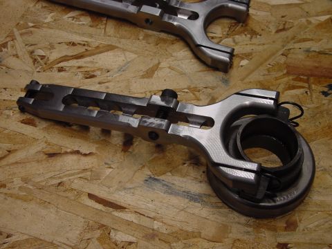 1979 Ford Bronco - Close-up of a metal clutch fork and release bearing assembly, resting on a textured wooden background.
