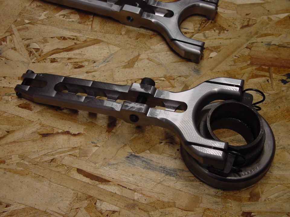 Metal clutch fork with attached release bearing, viewed from above on a wooden surface