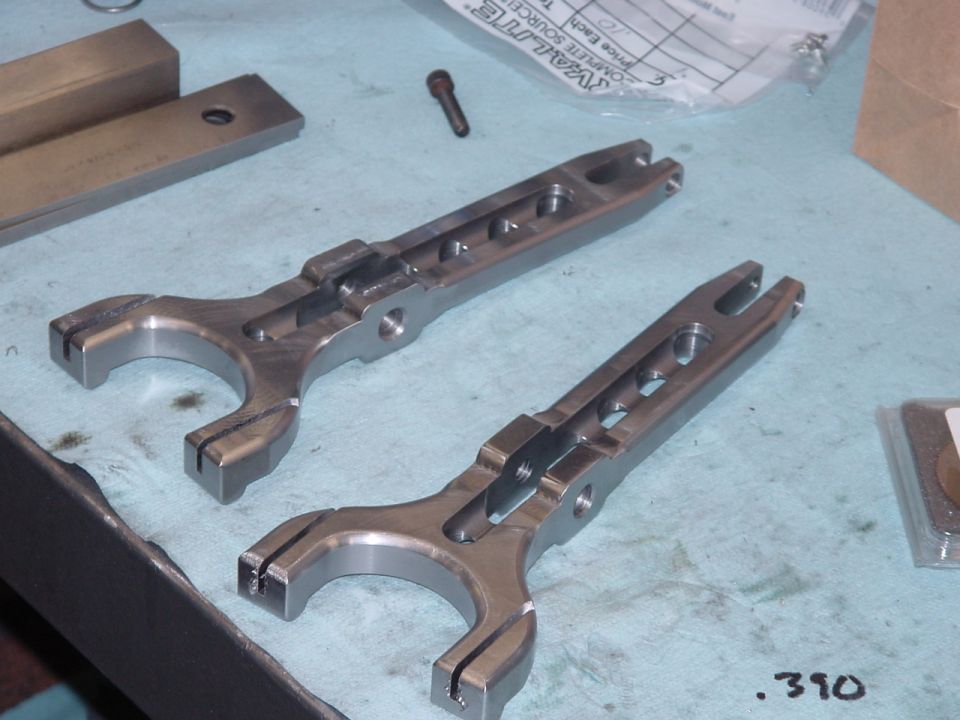 Two metal clutch fork parts on a workbench. .390 visible
