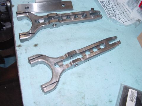 1979 Ford Bronco - Close-up of two machined metal clutch fork components resting on a light blue surface, with some packaging visible.
