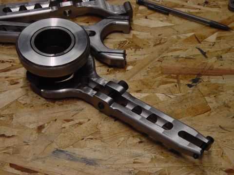 1979 Ford Bronco - A metal clutch fork and bearing assembly are shown on a workbench, with a pen in the background.