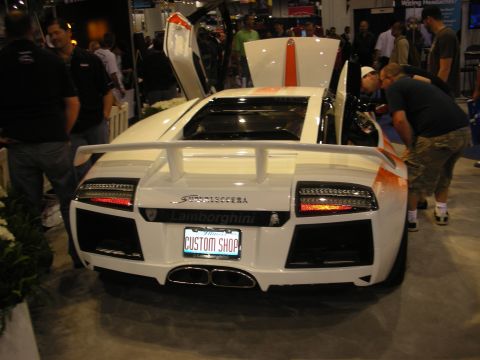 1998 Ford Crown Victoria - Rear view of a white Lamborghini Murcielago with raised doors and a Custom Shop license plate at a busy show.