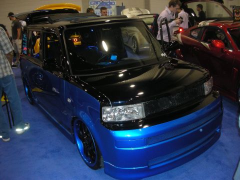 1998 Ford Crown Victoria - two-tone black and blue Scion xB boxy hatchback sits lowered on dark wheels among other cars at a show.