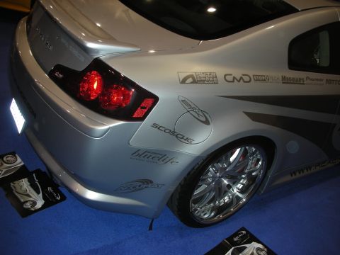 1998 Ford Crown Victoria - Rear three-quarter of a silver coupe covered in sponsor decals, sitting on large chrome wheels at an indoor display.