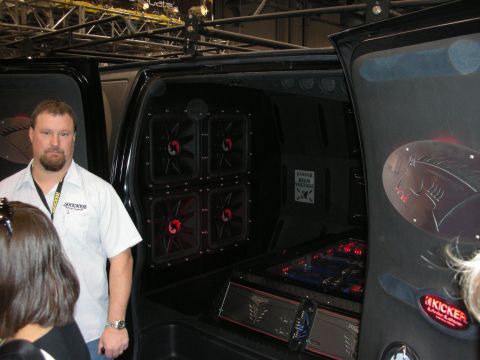 1998 Ford Crown Victoria - man in a white polo stands by a black vehicle's open side showing four red-illuminated amps and Kicker audio gear.