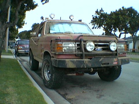 1989 Ford Bronco - This weathered Ford Bronco, possibly from the late 80s, sits on a residential street with a second vehicle in the background.