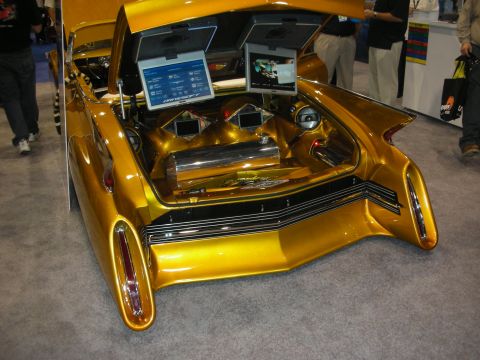 1998 Ford Crown Victoria - Rear of a gold custom car with hood and trunk open, showing twin LCD screens and chrome audio gear at a show.