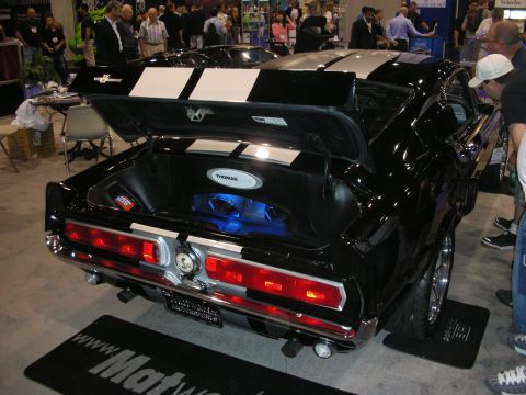 1998 Ford Crown Victoria - rear of a black striped Mustang fastback with its trunk open is surrounded by a crowd on a Matworld mat at a show.