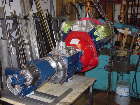 1979 Ford Bronco - A rebuilt engine and transmission assembly, painted red and blue, is hoisted by chains in a workshop setting.
