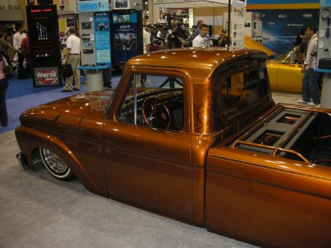 1998 Ford Crown Victoria - lowered copper-orange custom pickup with wire wheels sits on a show floor near a Sirius display booth.