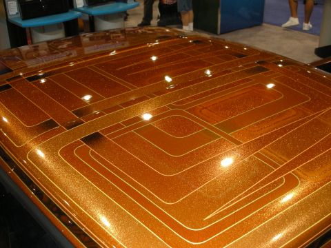 1998 Ford Crown Victoria - glossy copper metalflake surface is decorated with concentric pinstriped square patterns reflecting overhead lights.