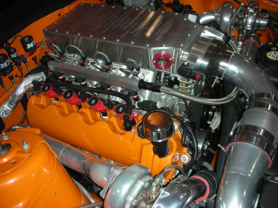 Close-up of twin-turbo orange V8 engine with polished piping and braided fuel lines
