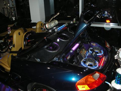 1998 Ford Crown Victoria - open trunk of a dark convertible is packed with subwoofers and neon-lit audio components on display.