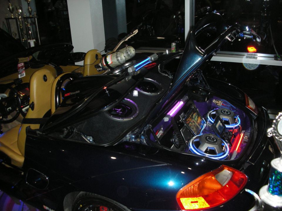 Open trunk of a dark convertible packed with subwoofers and neon-lit audio gear