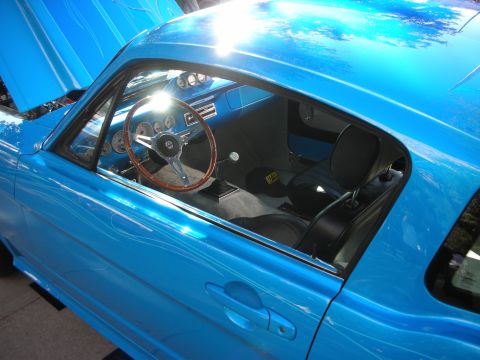 1998 Ford Crown Victoria - Through the side window of a bright blue classic coupe, a wood-rimmed wheel, gauges and black bucket seats are visible.
