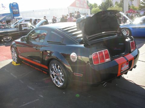 1998 Ford Crown Victoria - black Shelby GT500 Mustang shown rear three-quarter with red racing stripes and both hood and trunk open at an event.