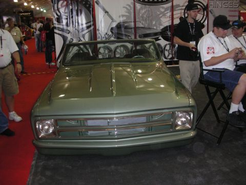 1998 Ford Crown Victoria - pale green lowered classic Chevrolet C10-style pickup shown front-on at an indoor booth with billet grille and people seated nearby.
