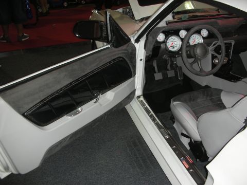 1998 Ford Crown Victoria - View through the open door of a white custom car showing a carbon-fiber door panel, gray seat, and white-faced gauge cluster.