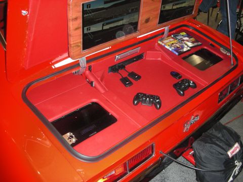 1998 Ford Crown Victoria - Red car's trunk customized into a gaming and media station with game controllers, screens, and storage compartments.