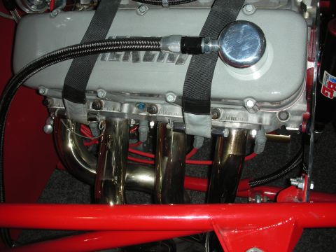 1998 Ford Crown Victoria - Engine valve cover and tubular headers held with seat-belt straps, mounted above a red tubular chassis.