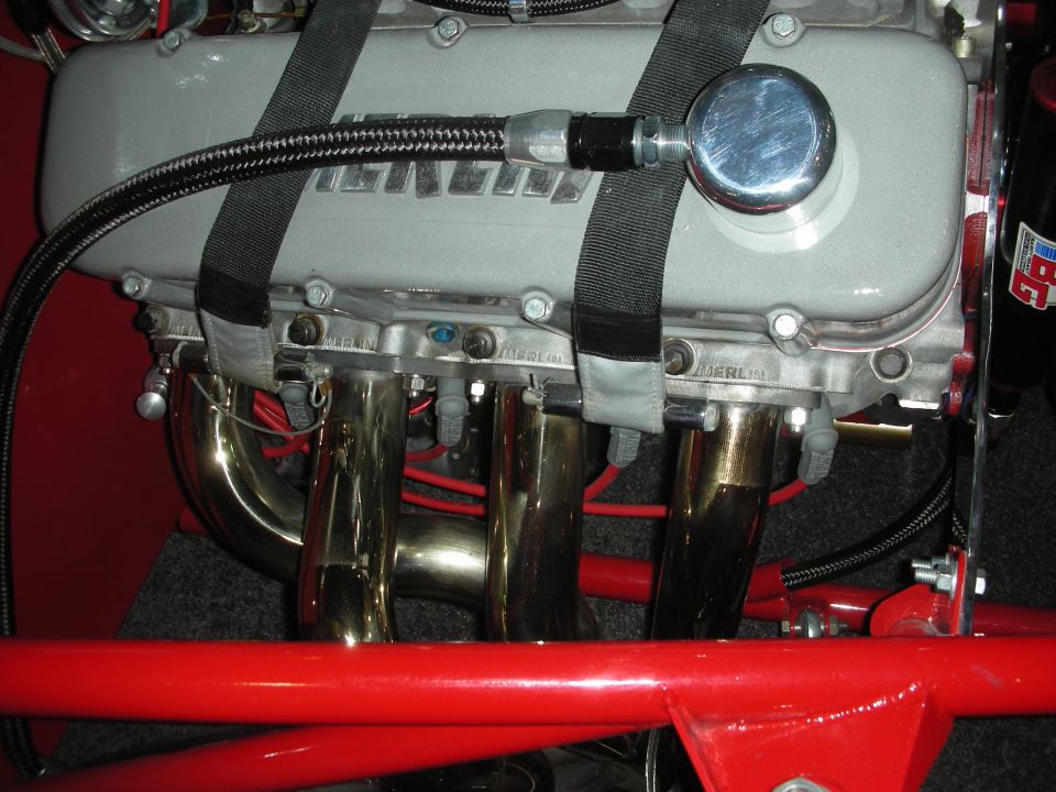 Aluminum valve cover and headers wrapped with seat-belt straps over a red frame